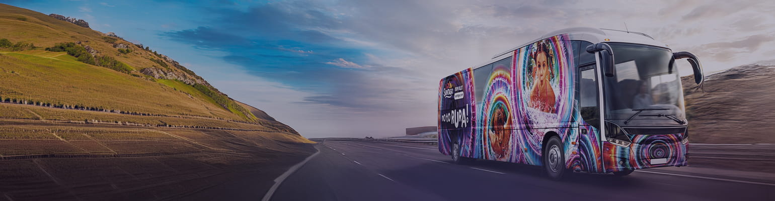 Suntago bus decorated with palm tree graphics. The side of the bus displays the text "Buy a ticket at parkofpoland.life". In the background, silhouettes of palm trees against the setting sun.