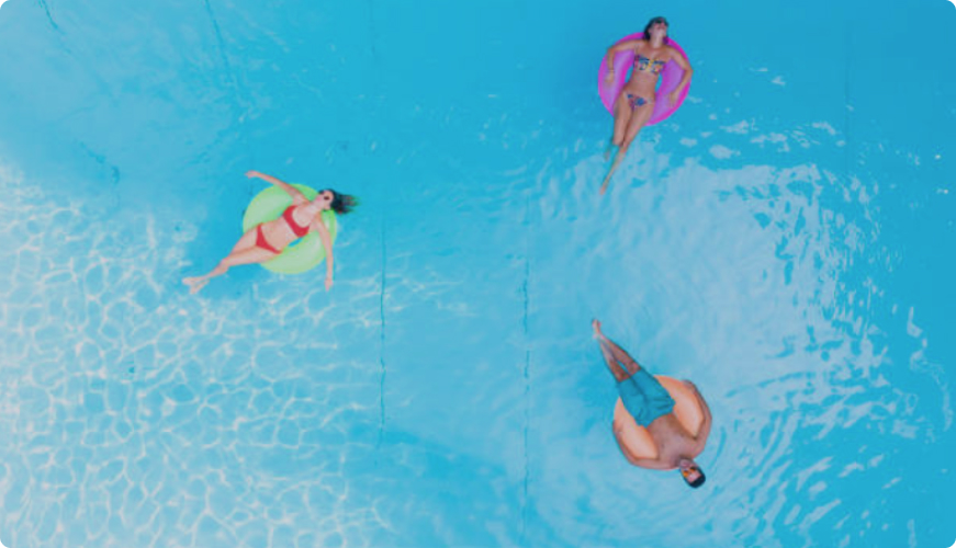 Three people relax and float in the pool on colorful floaties.
