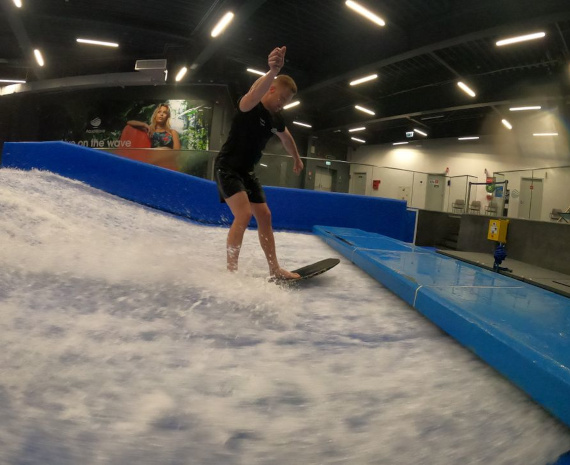 A man surfing on a wave in an indoor water park amidst splashing water.