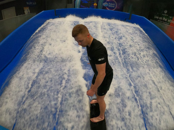 A man surfing on a wave in an indoor water park amidst splashing water.