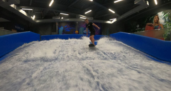 A man surfing on a wave in an indoor water park amidst splashing water.